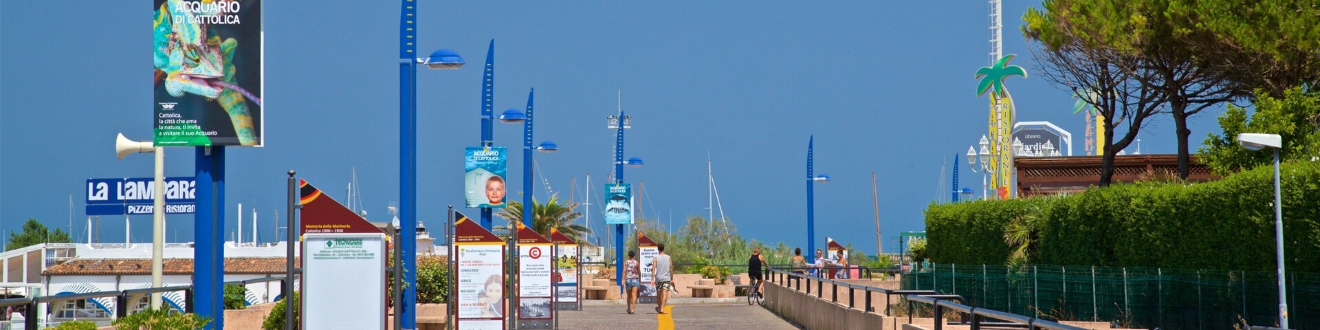 A coastal promenade with blue street lamps, informational signs, and a yellow path.