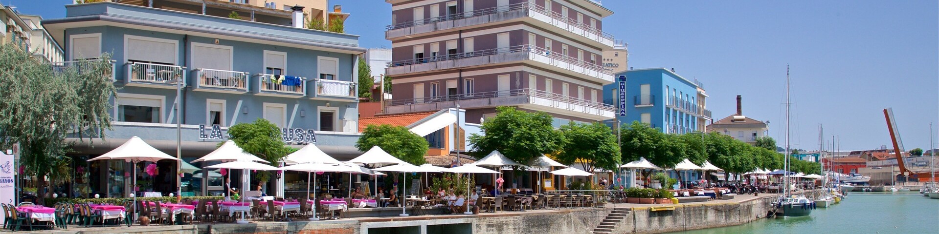 A waterfront with outdoor seating, boats, and colorful buildings.
