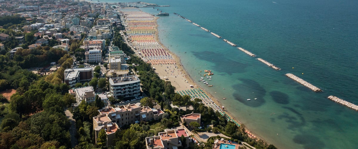 An aerial view of a coastal city with a long beach, clear blue waters, and a pier extending into the sea.