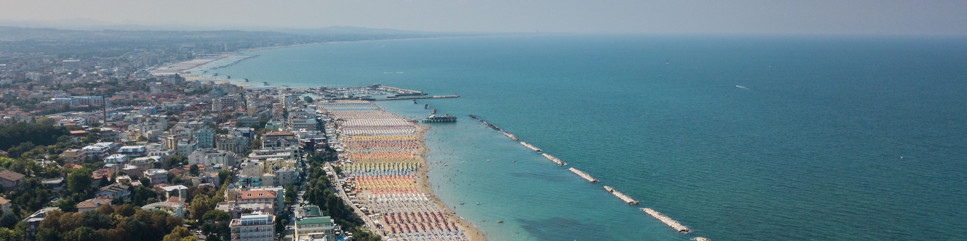 An aerial view of a coastal city with a long beach, clear blue waters, and a pier extending into the sea.