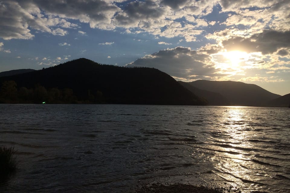 Ein See mit Bergen im Hintergrund und der untergehenden oder aufgehenden Sonne.