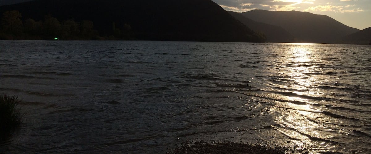 A lake with mountains in the background and the sun setting or rising.