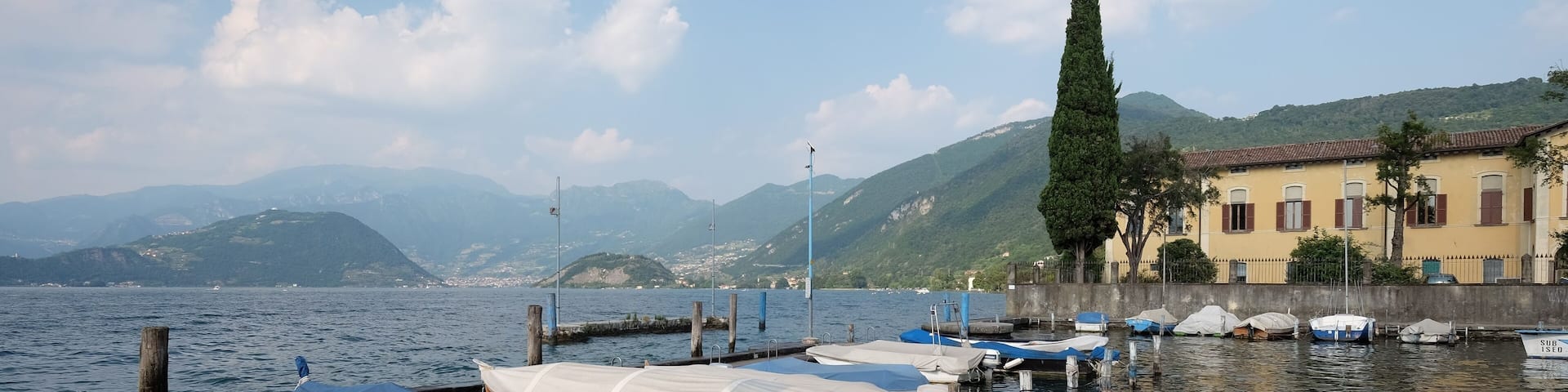 A calm lake with several boats docked at the pier, surrounded by mountains and a clear sky.