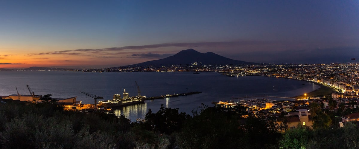 A coastal city at dusk with a prominent mountain in the background.