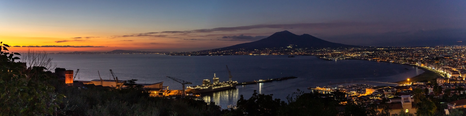 A coastal city at dusk with a prominent mountain in the background.