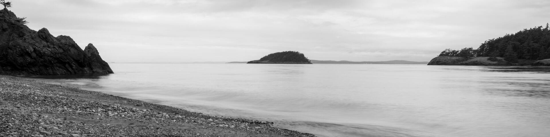 A pebbly beach with rocky outcrops and a distant island.