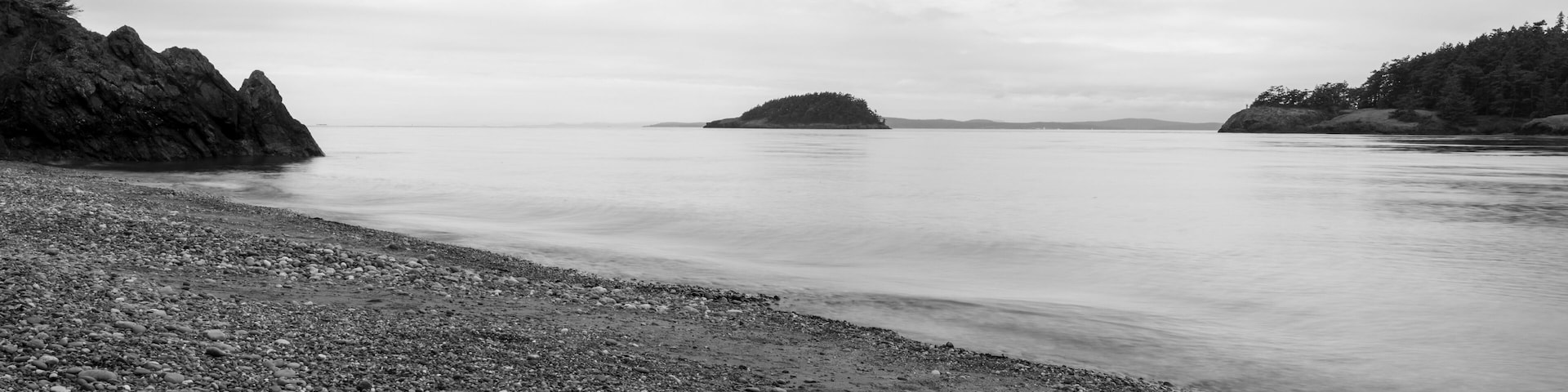 Ein kiesiger Strand mit Felsformationen und einer entfernten Insel.