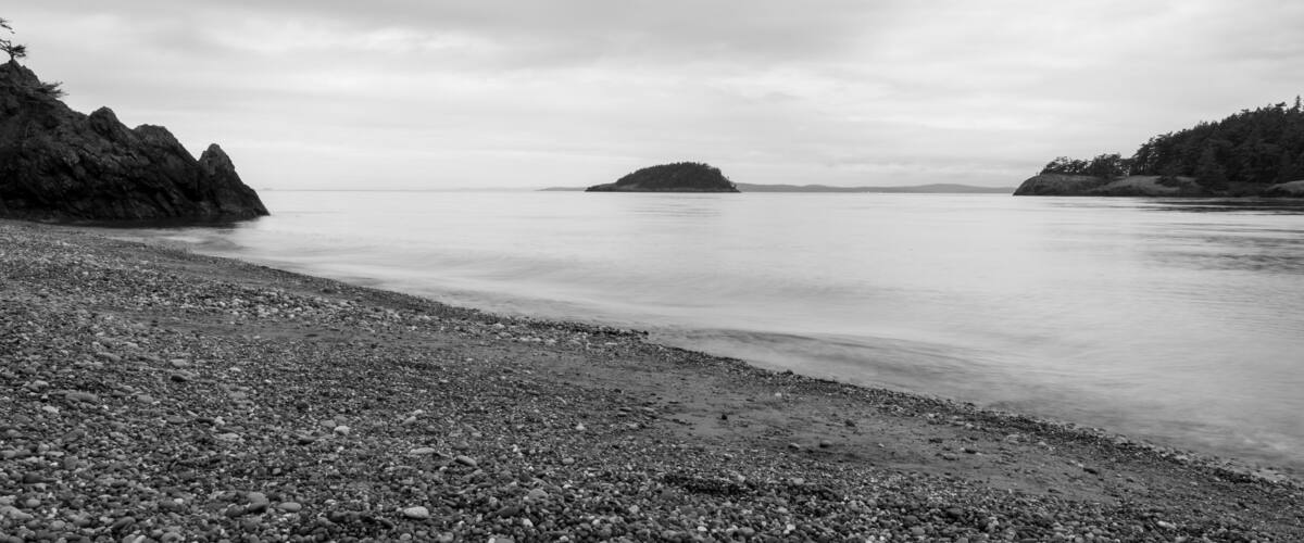 A pebbly beach with rocky outcrops and a distant island.