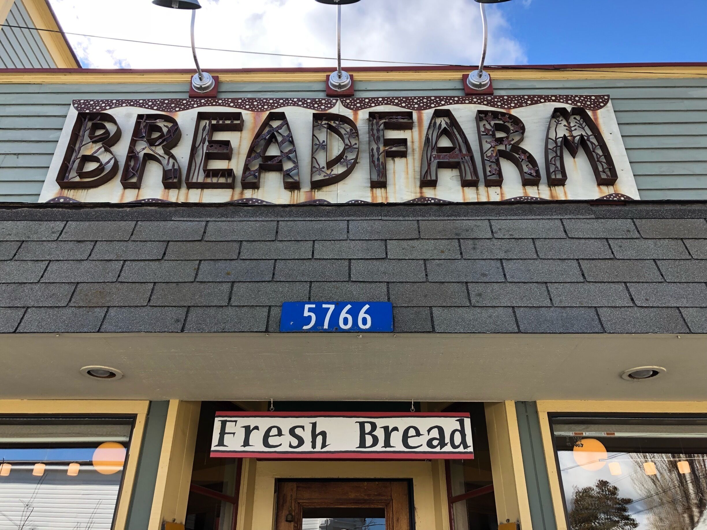 A storefront with a rustic metal sign reading "BREADFARM" and a blue street sign with the number "5766".