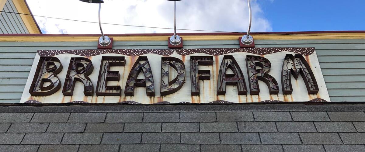 A storefront with a rustic metal sign reading "BREADFARM" and a blue street sign with the number "5766".