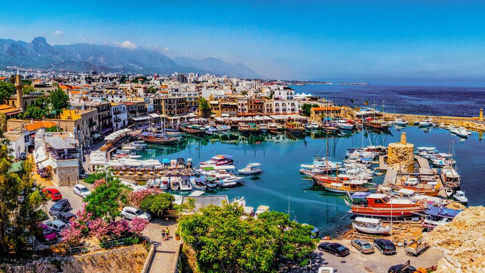 A coastal town with a marina, boats, and a mountainous backdrop.