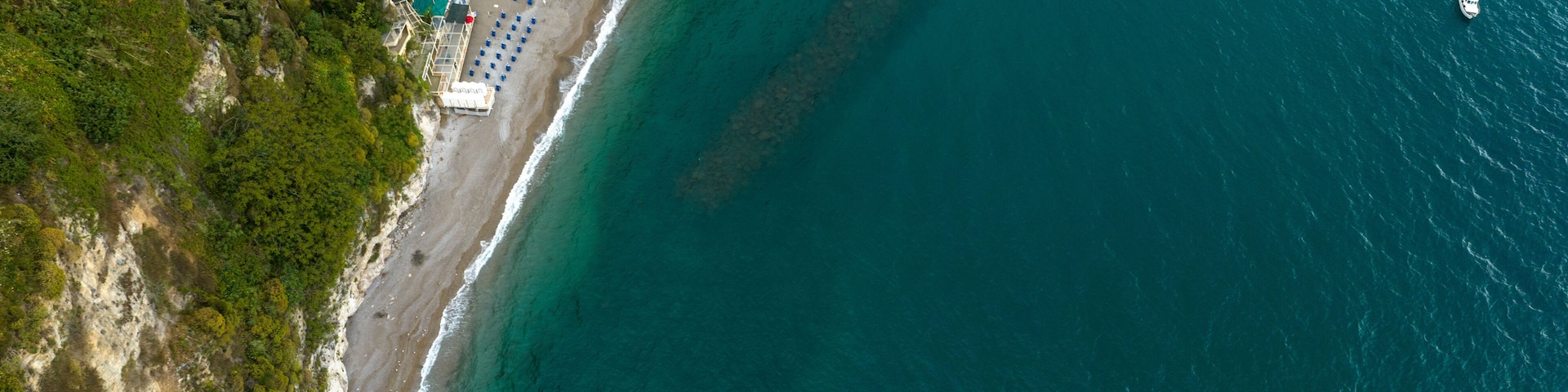 Vista aérea de uma área costeira com praia, piscina e barco na água.