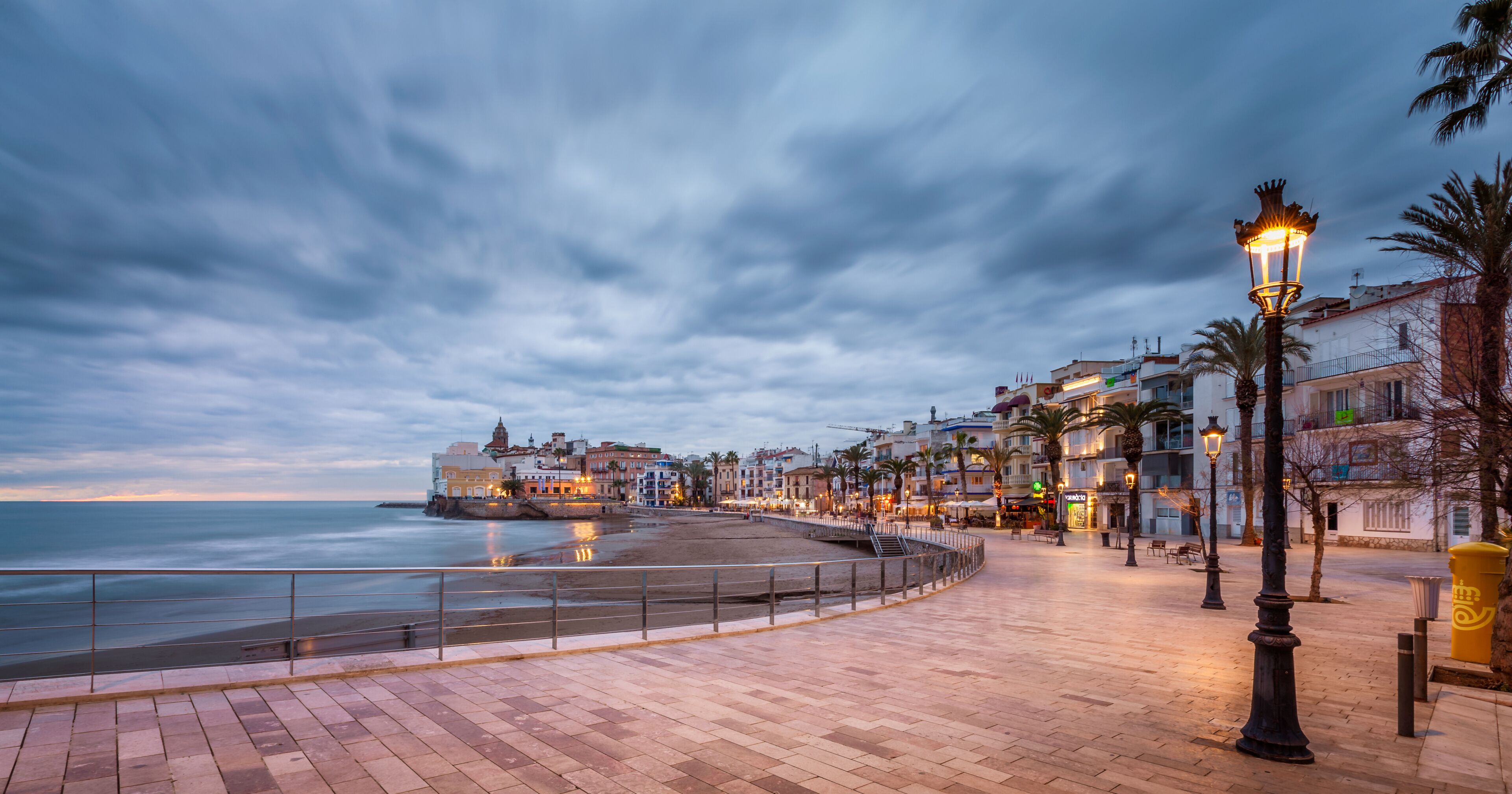 A coastal promenade with a sea view, a promenade with a railing, and buildings along the waterfront.