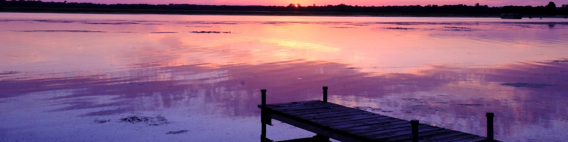 A sunset over a calm lake with a wooden dock extending into the water.