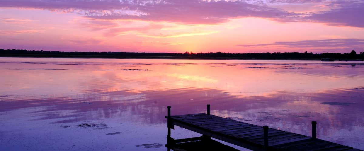 A sunset over a calm lake with a wooden dock extending into the water.