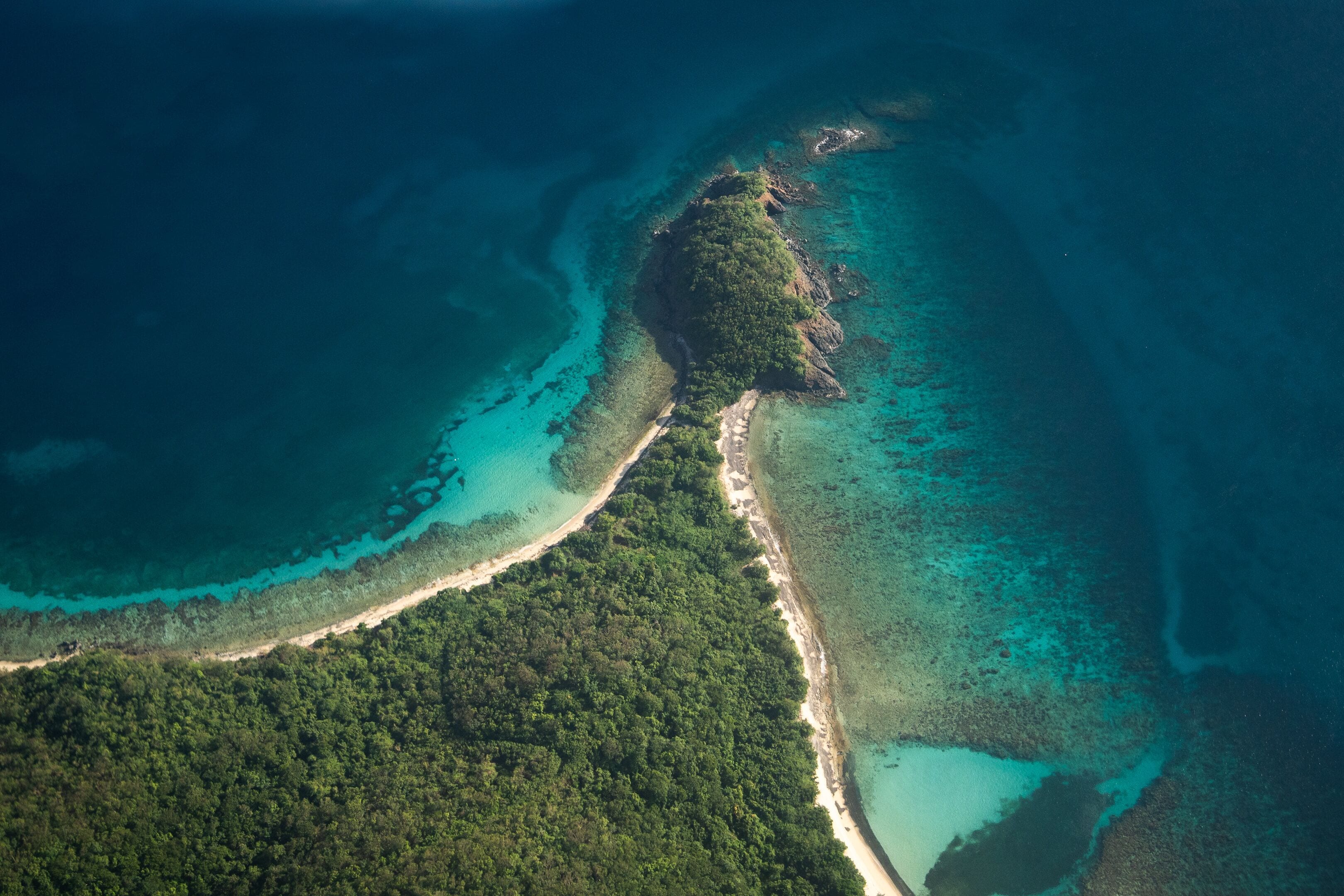 Vista aérea de una isla tropical con una playa estrecha, bosque denso y aguas turquesas cristalinas.