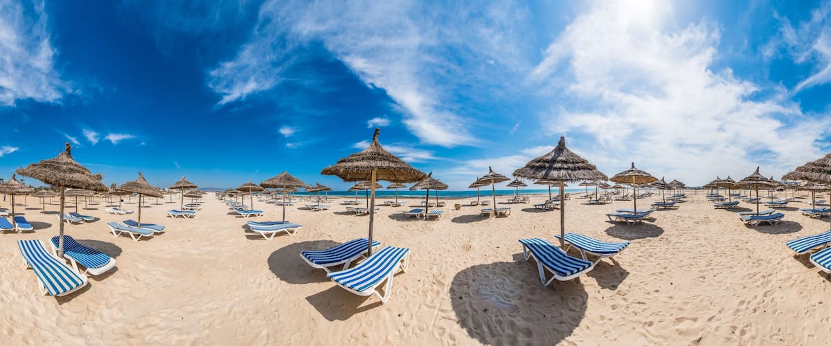 A beach with striped sun loungers and thatched umbrellas under a clear blue sky.