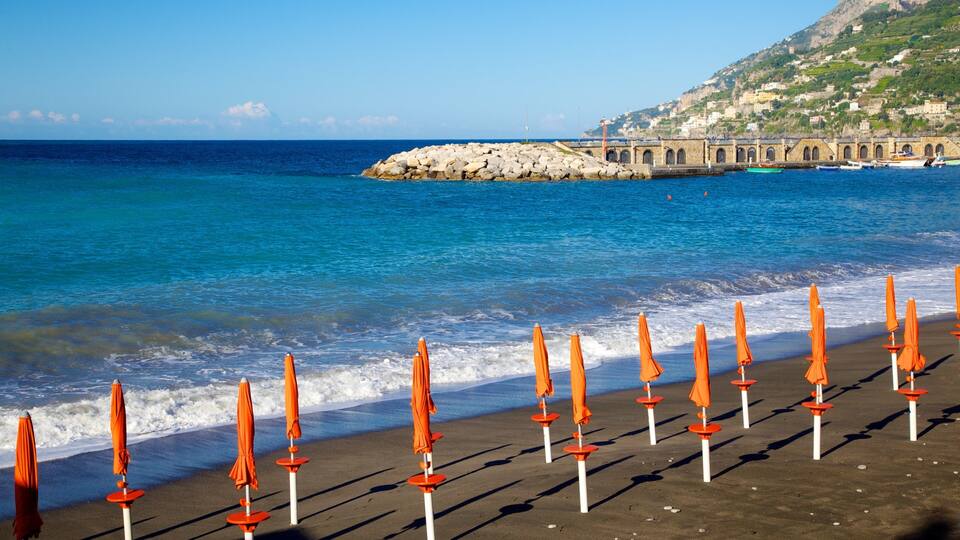 A beach with orange umbrellas and a rocky breakwater in the background.