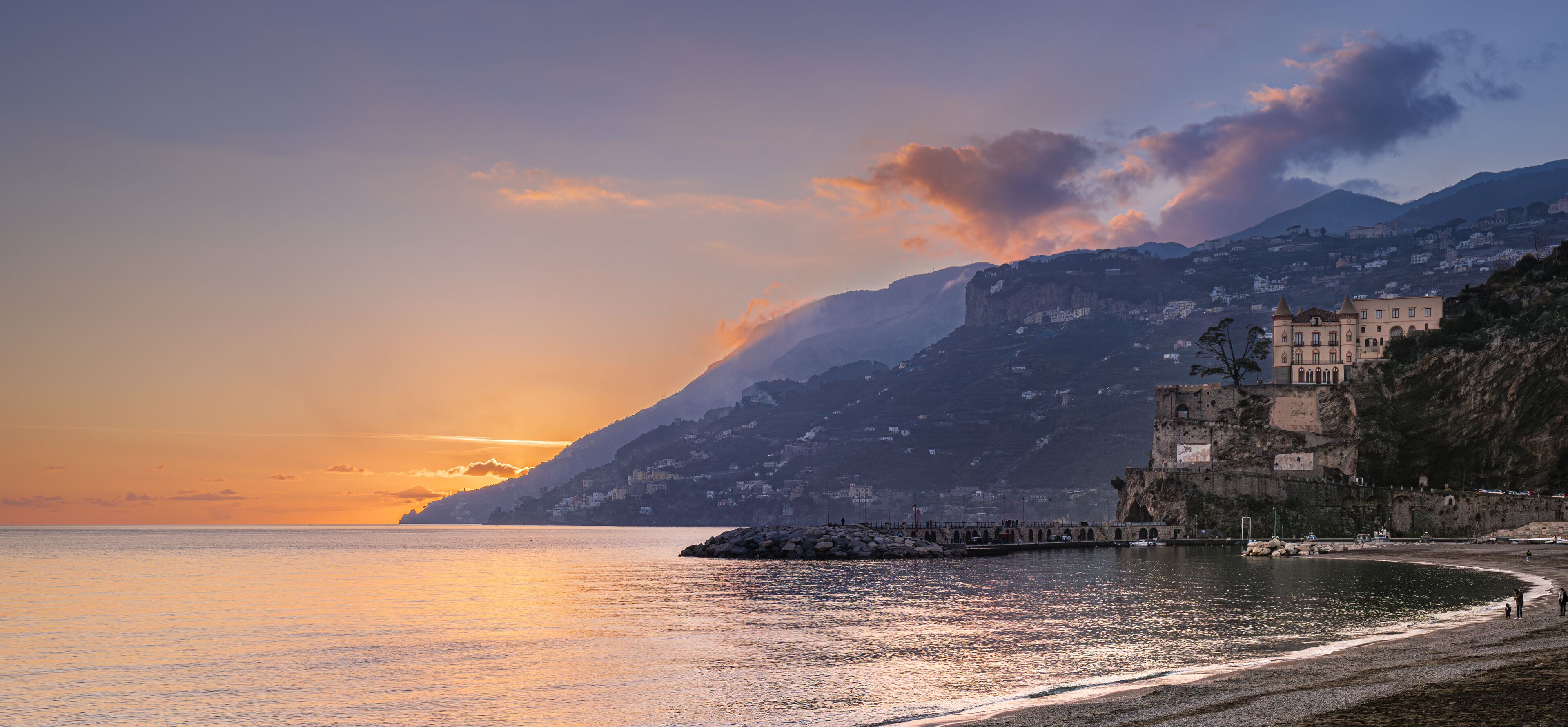 A coastal sunset with a mountain and a historic building.
