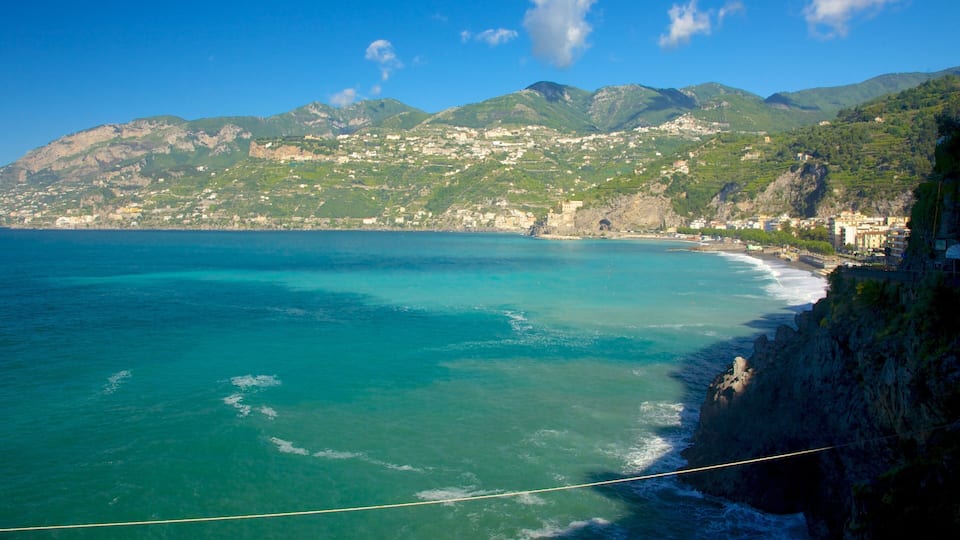 A coastal town with a clear blue sea, a rocky shoreline, and a mountainous backdrop.