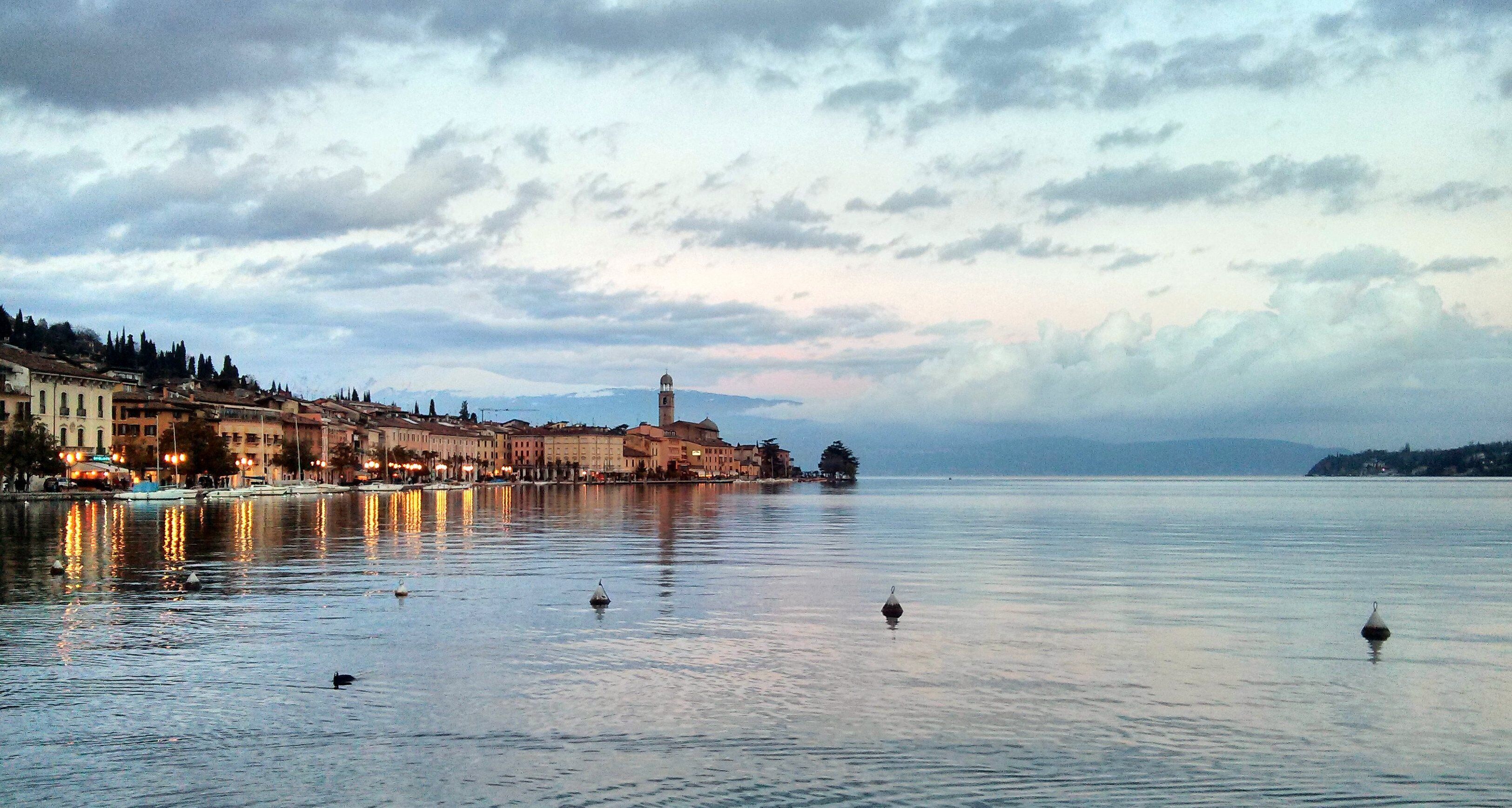 A calm lake with buildings along the shore and a tower in the distance.