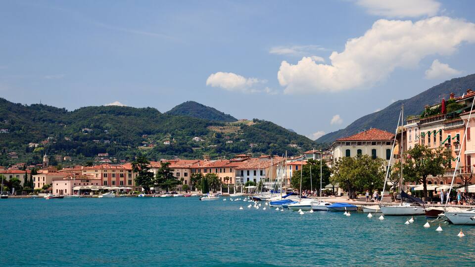 A coastal town with boats docked along the waterfront, surrounded by hills and traditional buildings.