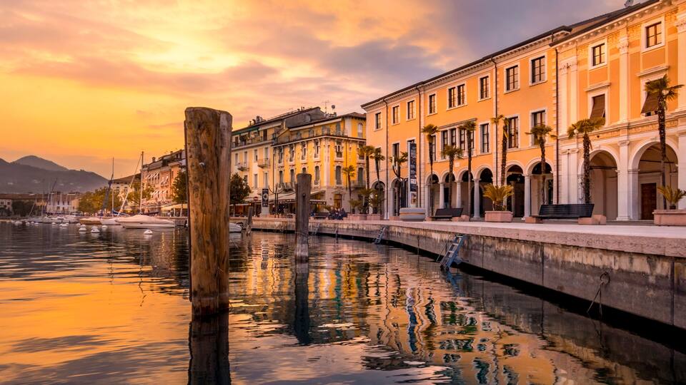 A waterfront with buildings, a wooden post, and a calm river reflecting the sky.