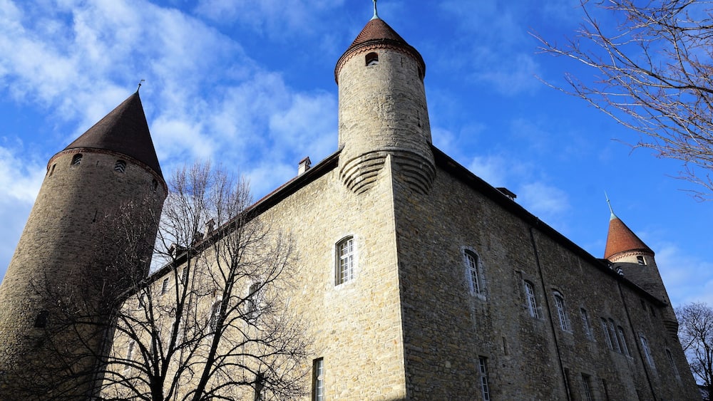Un bâtiment historique en pierre, doté de deux tours imposantes, se dressant sous un ciel d’un bleu éclatant.