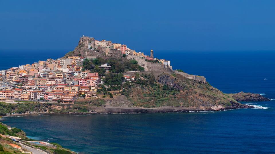 A coastal town with colorful buildings, a prominent hilltop fortress, and the ocean.