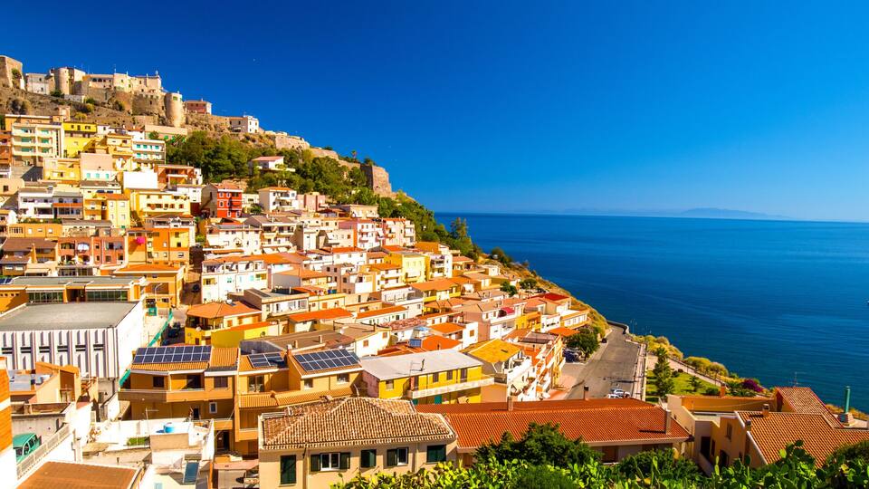 A coastal town with colorful buildings, a hilltop fortress, and the sea.