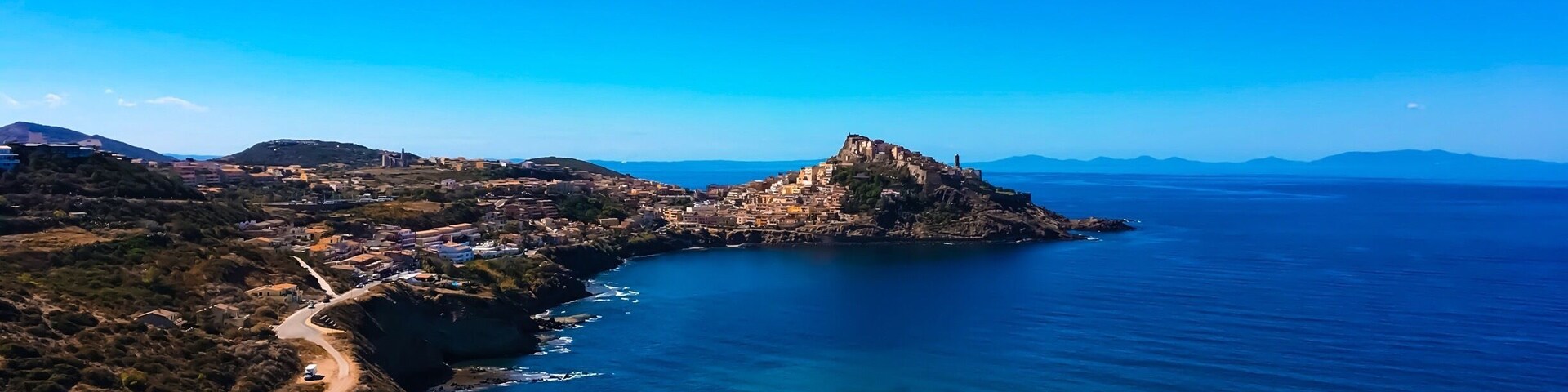 Un paisaje costero con una estructura destacada en la cima de una colina, un camino sinuoso y un cielo azul despejado.