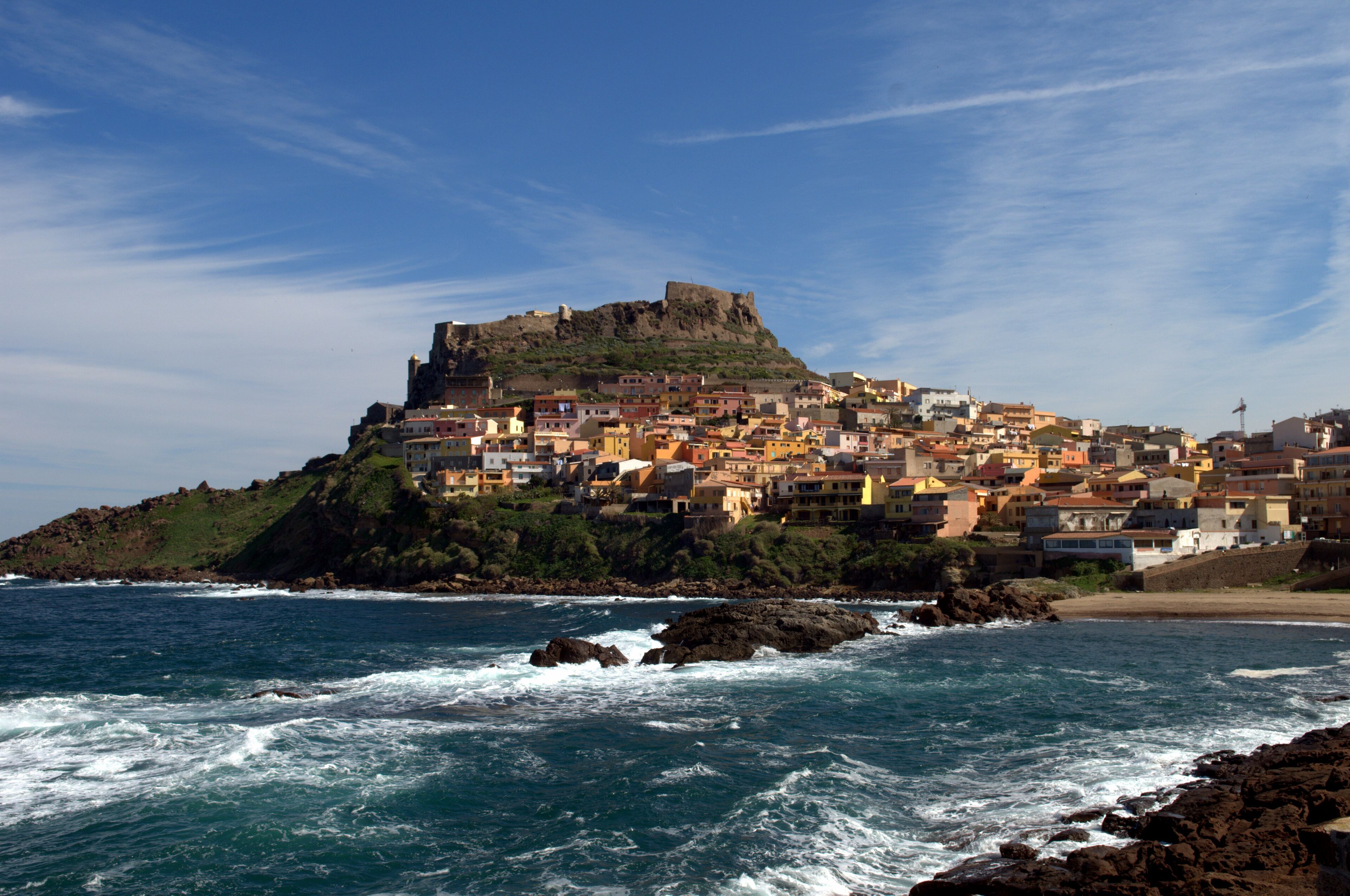 A coastal town with a prominent castle on a hill, surrounded by colorful buildings and rocky coastline.