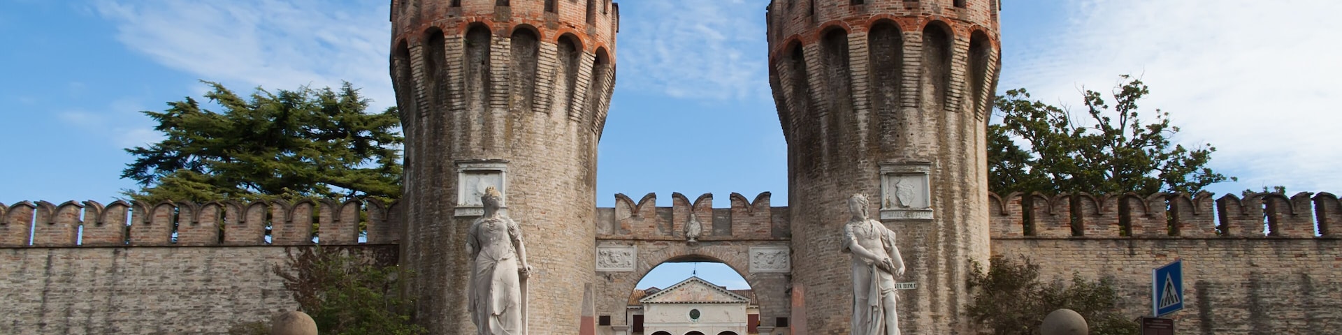 A historic gate with two tall towers and statues, leading to a building with arches.