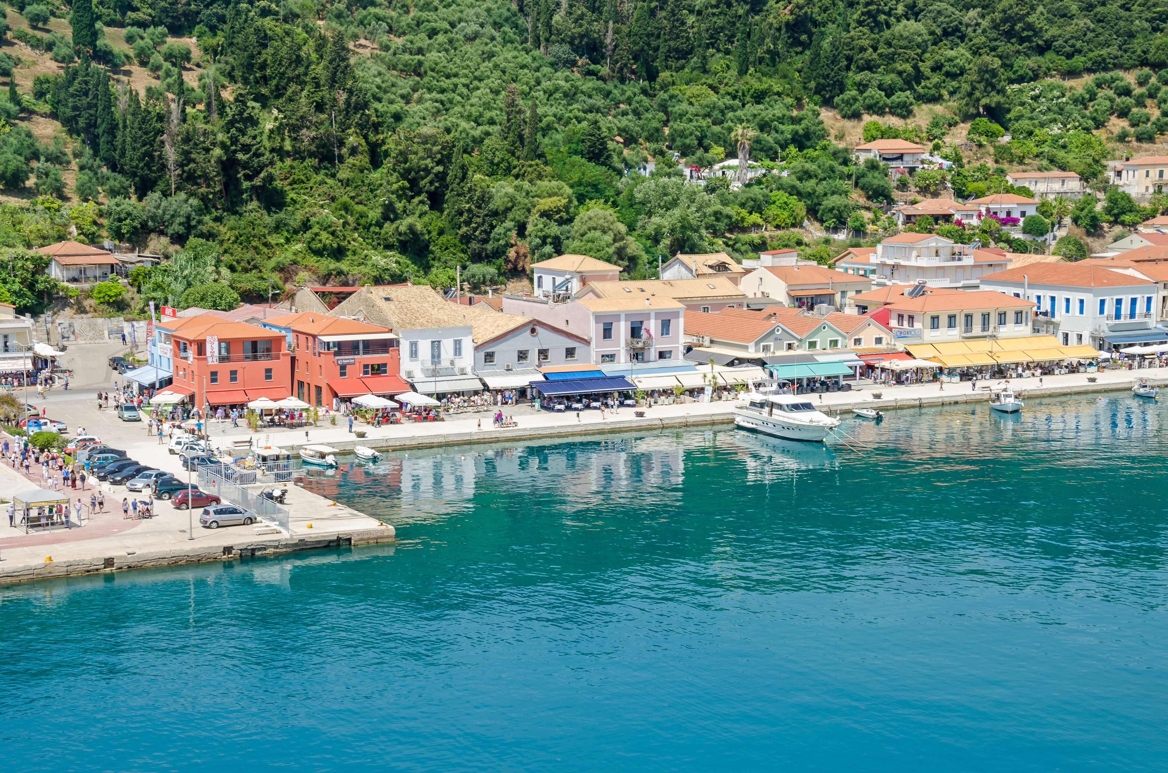 A coastal town with colorful buildings, a marina, and a hillside with trees.