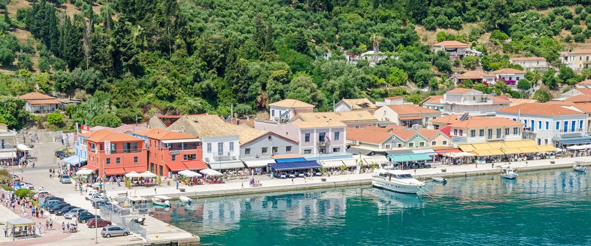 A coastal town with colorful buildings, a marina, and a hillside with trees.