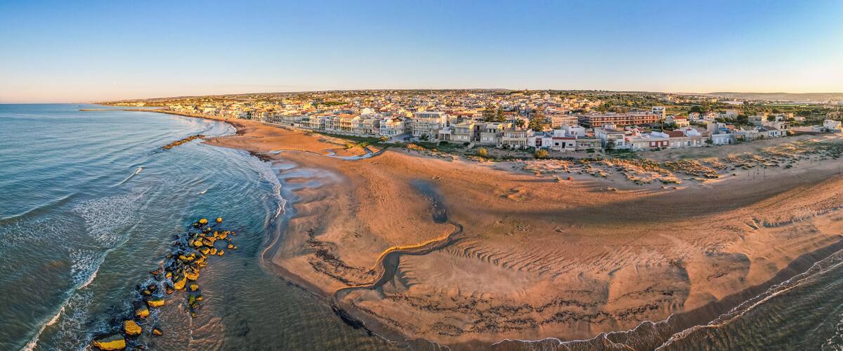 A coastal town with a beach, houses, and a clear sky.
