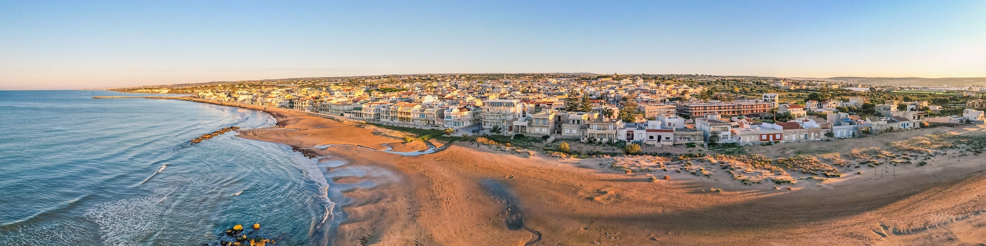A coastal town with a beach, houses, and a clear sky.