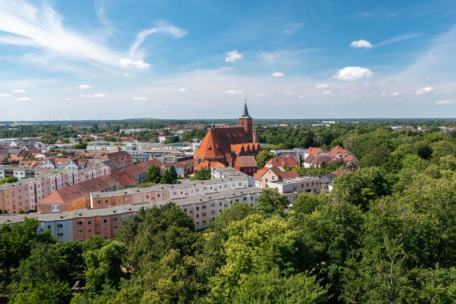 Eine Stadt mit einem markanten Kirchengebäude und einem hohen Kirchturm, umgeben von Wohnhäusern und üppigen Grünflächen.