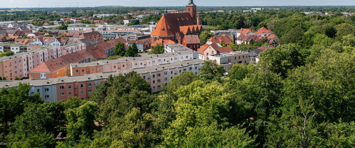 A town with a prominent church with a tall spire, surrounded by residential buildings and lush green trees.