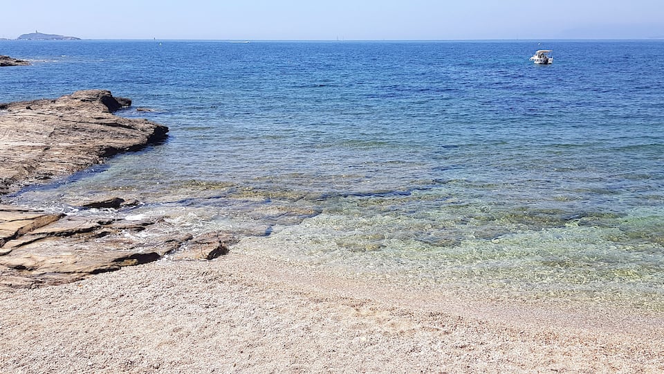 A rocky coastline with clear water and a boat in the distance.