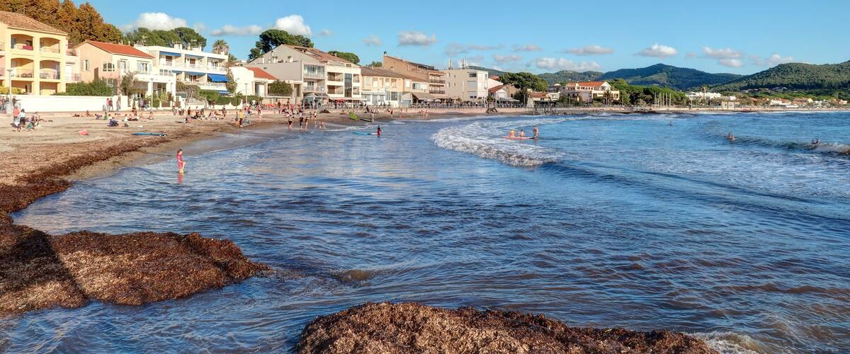 A coastal town with buildings along the shore, clear blue water, and rocky outcrops.