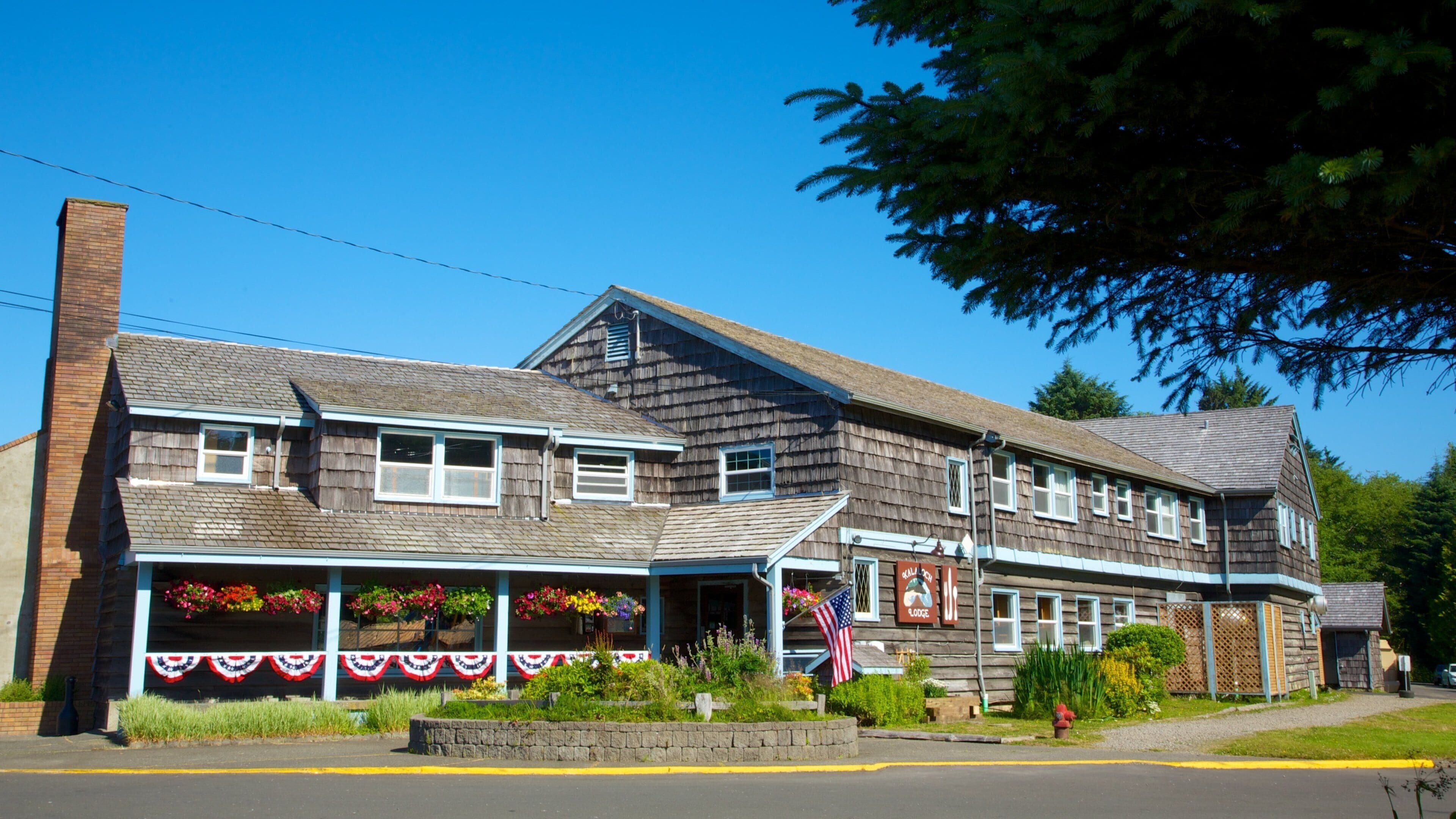 A wooden building with a porch decorated with flowers and an American flag.