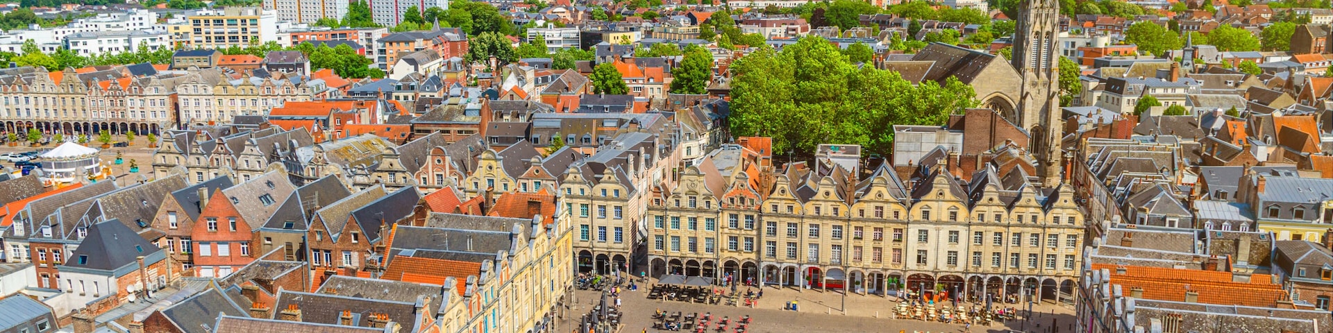 Uma cidade europeia histórica com uma igreja imponente, uma praça com cafés e um rio ao fundo.