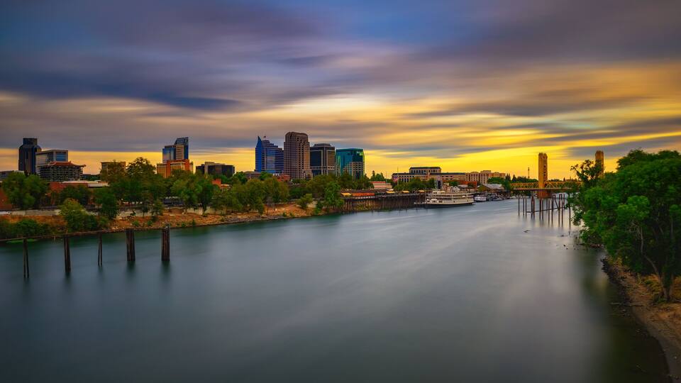 A river with a city skyline in the background, including modern buildings and a bridge.
