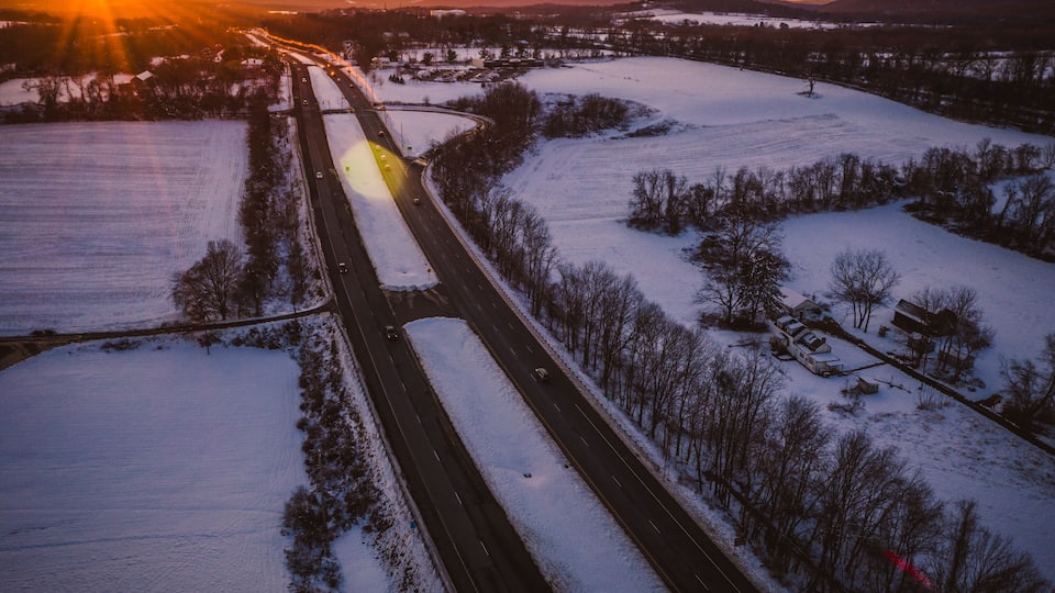 A highway curving through a snowy landscape with a sunset in the background.