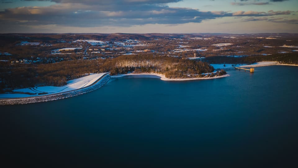 An aerial view of a coastal area with a large body of water, a snow-covered shoreline, and a bridge connecting two land masses.