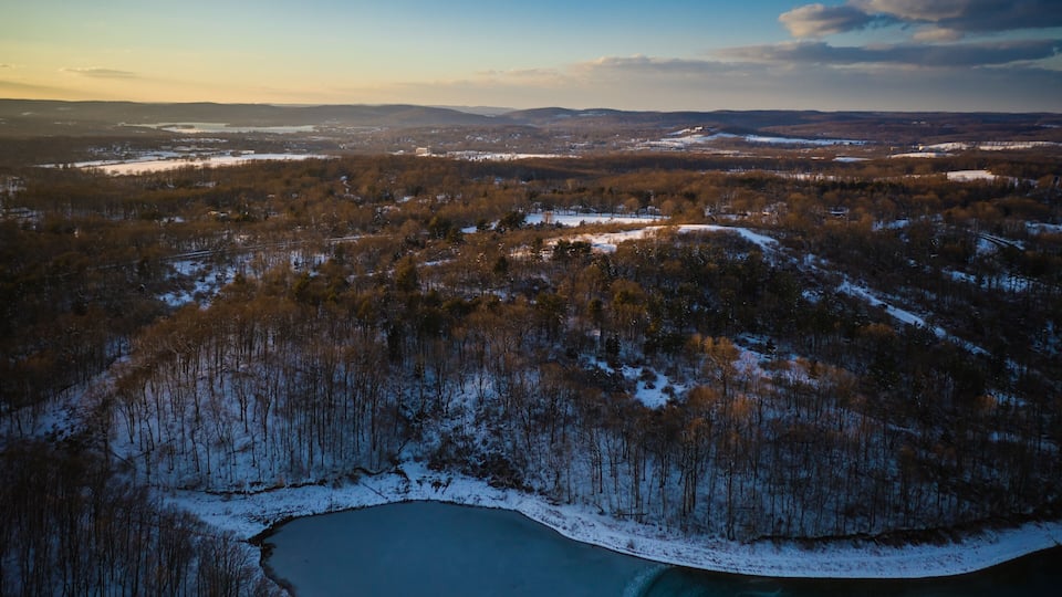 A winter landscape with a lake surrounded by snow-covered trees and distant mountains.