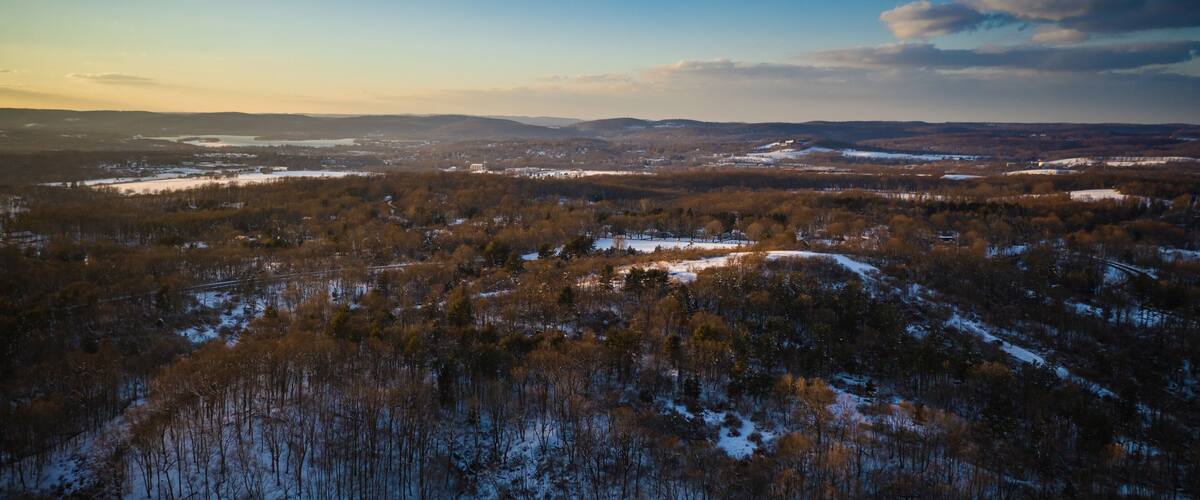 A winter landscape with a lake surrounded by snow-covered trees and distant mountains.