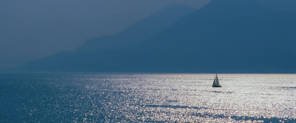 A sailboat on calm waters with a mountain range in the background.