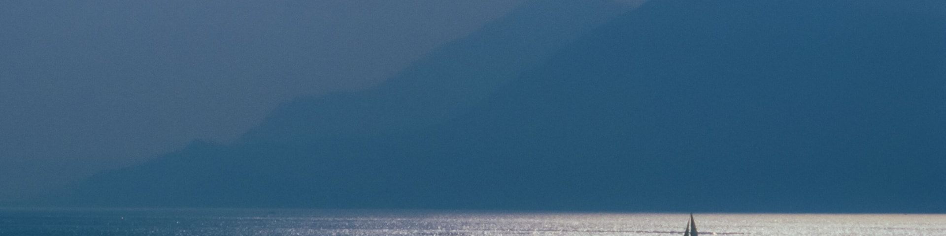 A sailboat on calm waters with a mountain range in the background.